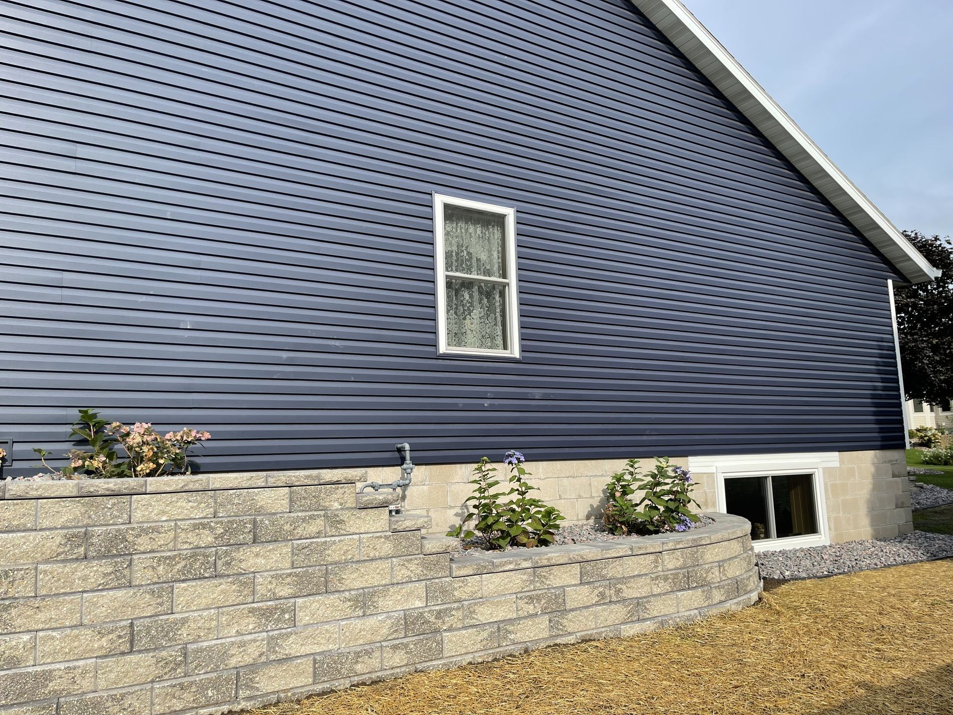 Blue house exterior with stone retaining wall, small window, and gravel landscaping