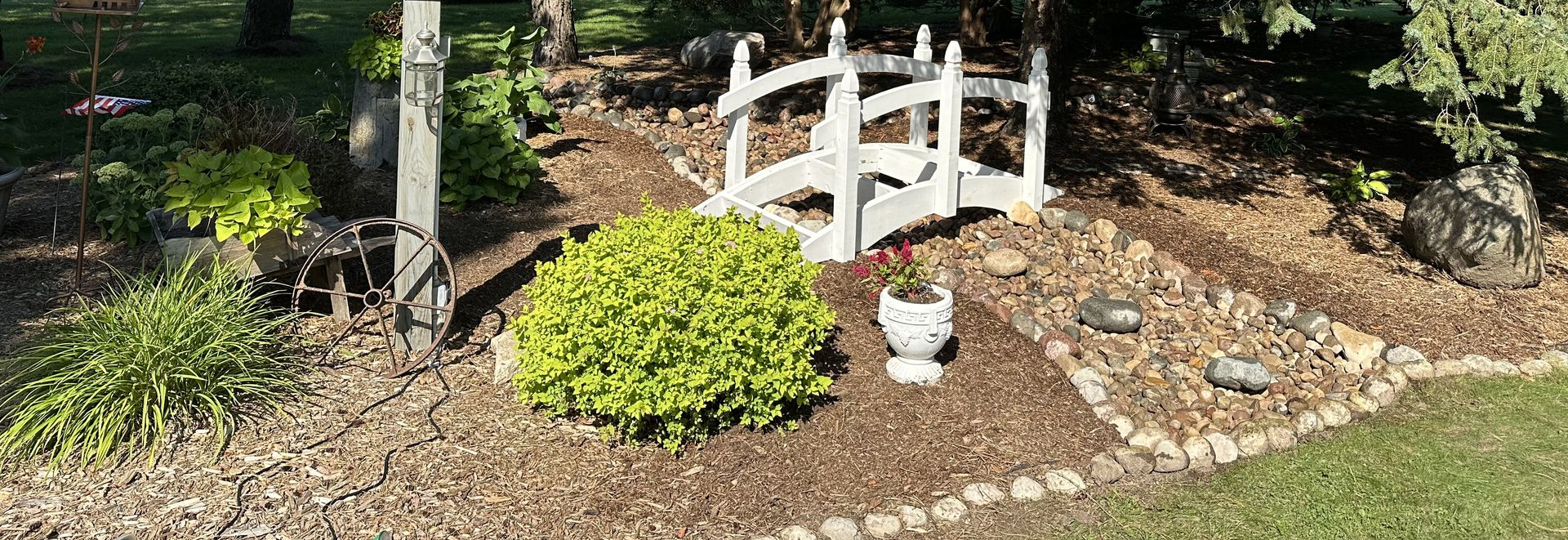Mulched garden bed with hostas and other green plants beside a grassy lawn