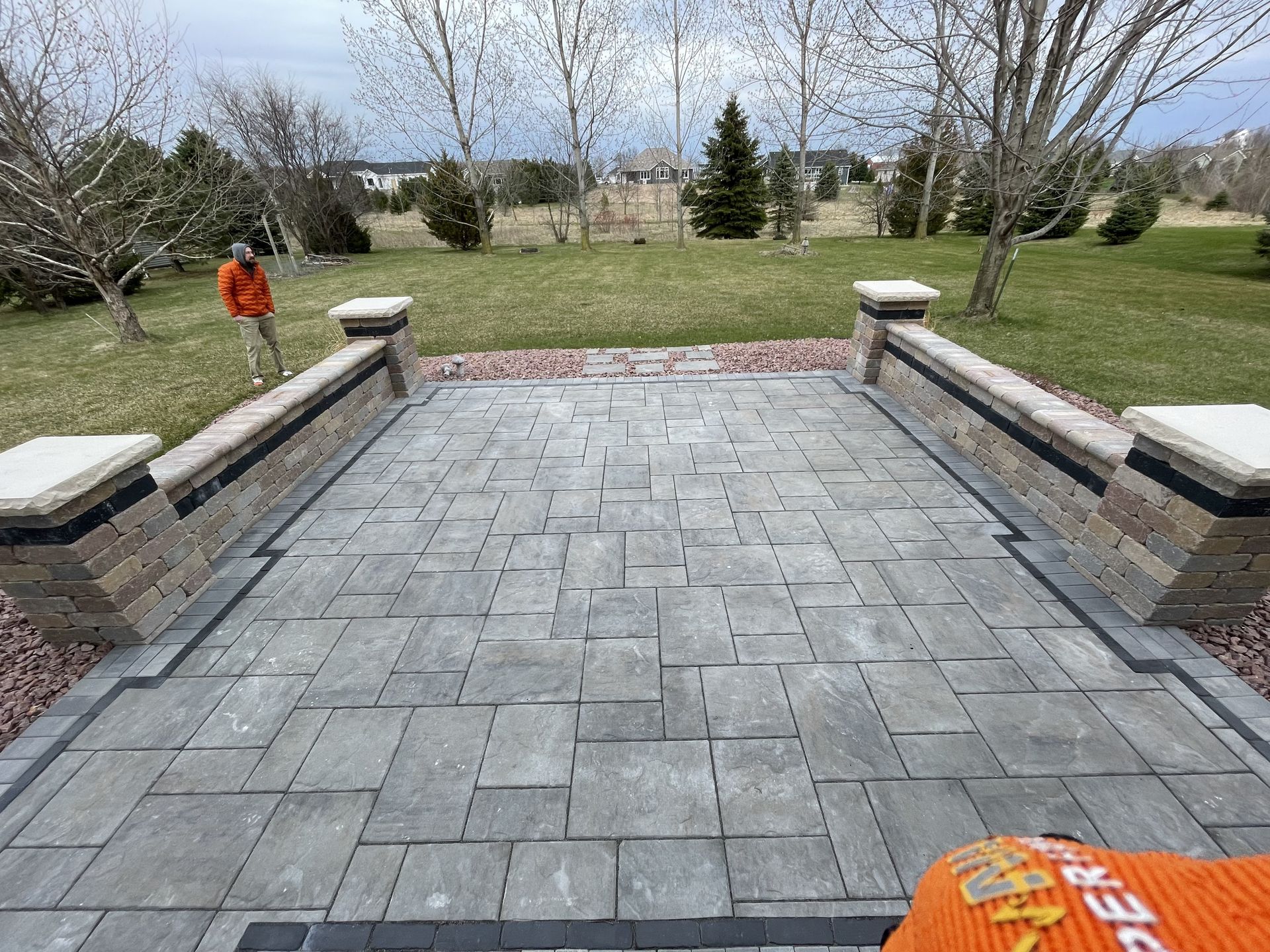 Stone patio wall with central steps leading to a house deck and glass sunroom, with potted plants on top