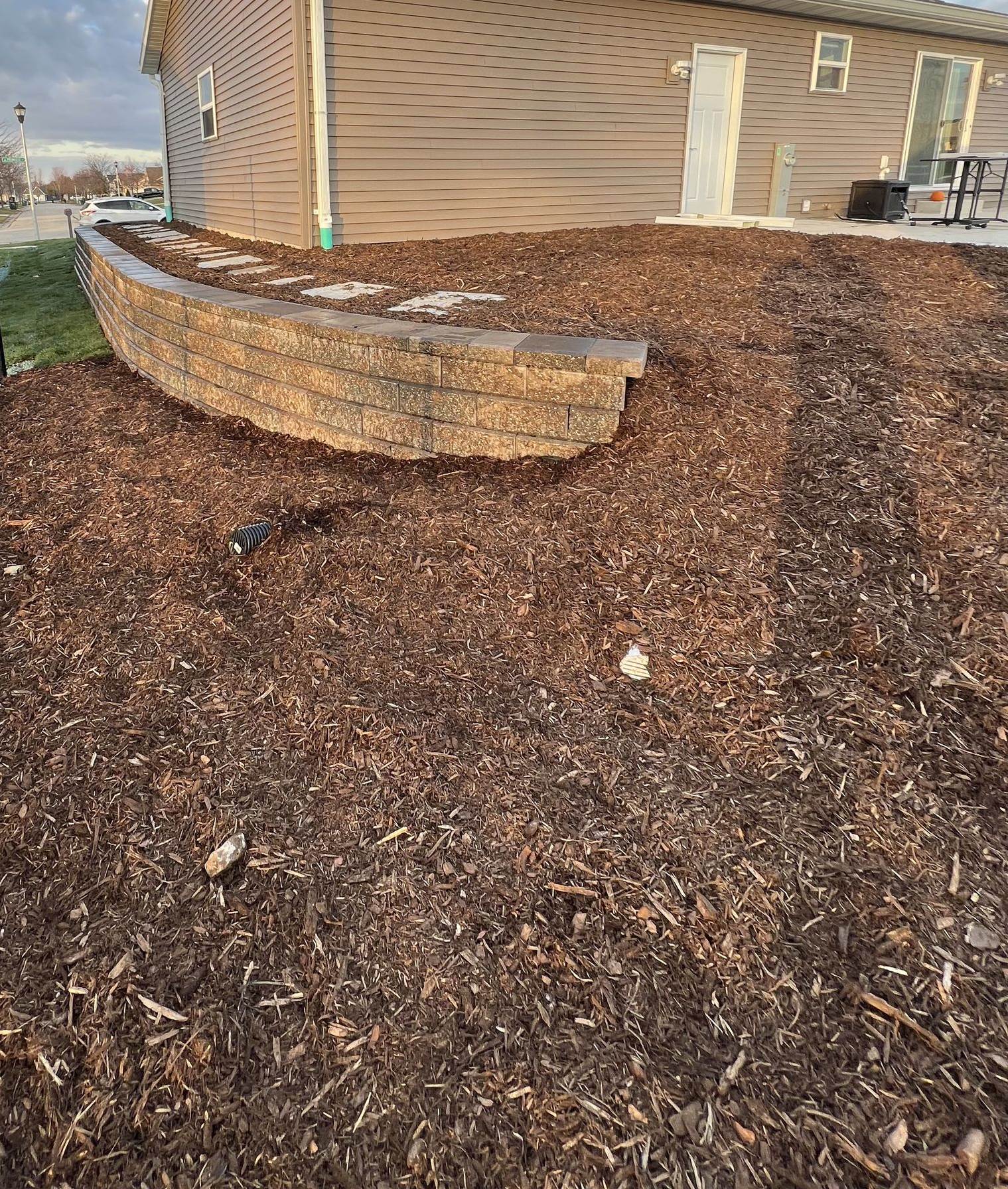 Garden bed with black mulch, large flat stones, colorful flowers, and green grass border