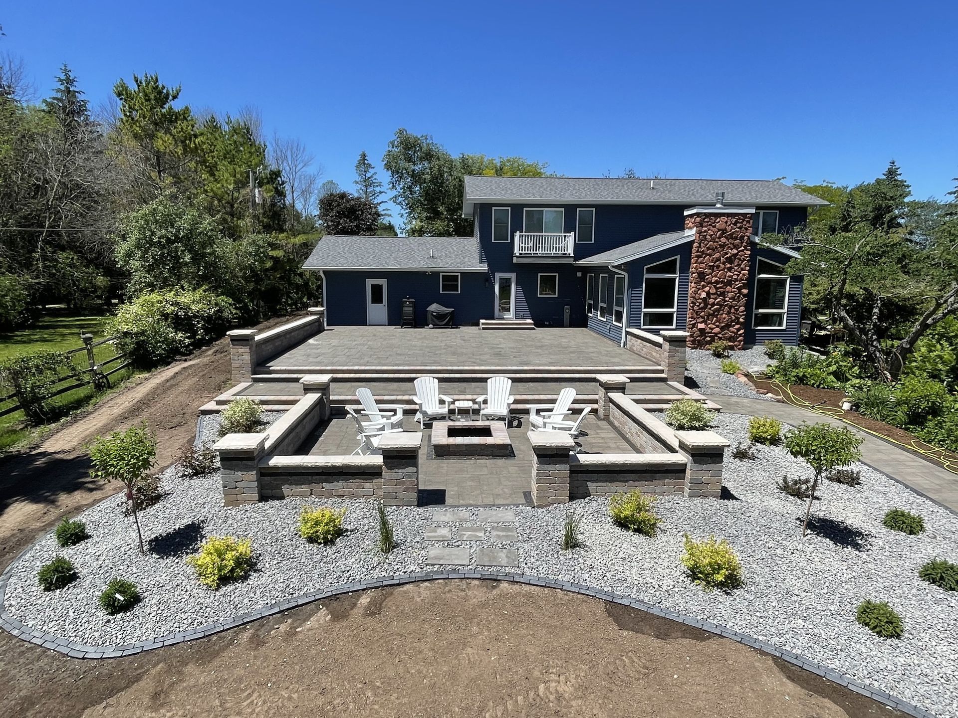 Backyard patio with stone seating, fire pit, gravel landscaping, and a modern house in the background