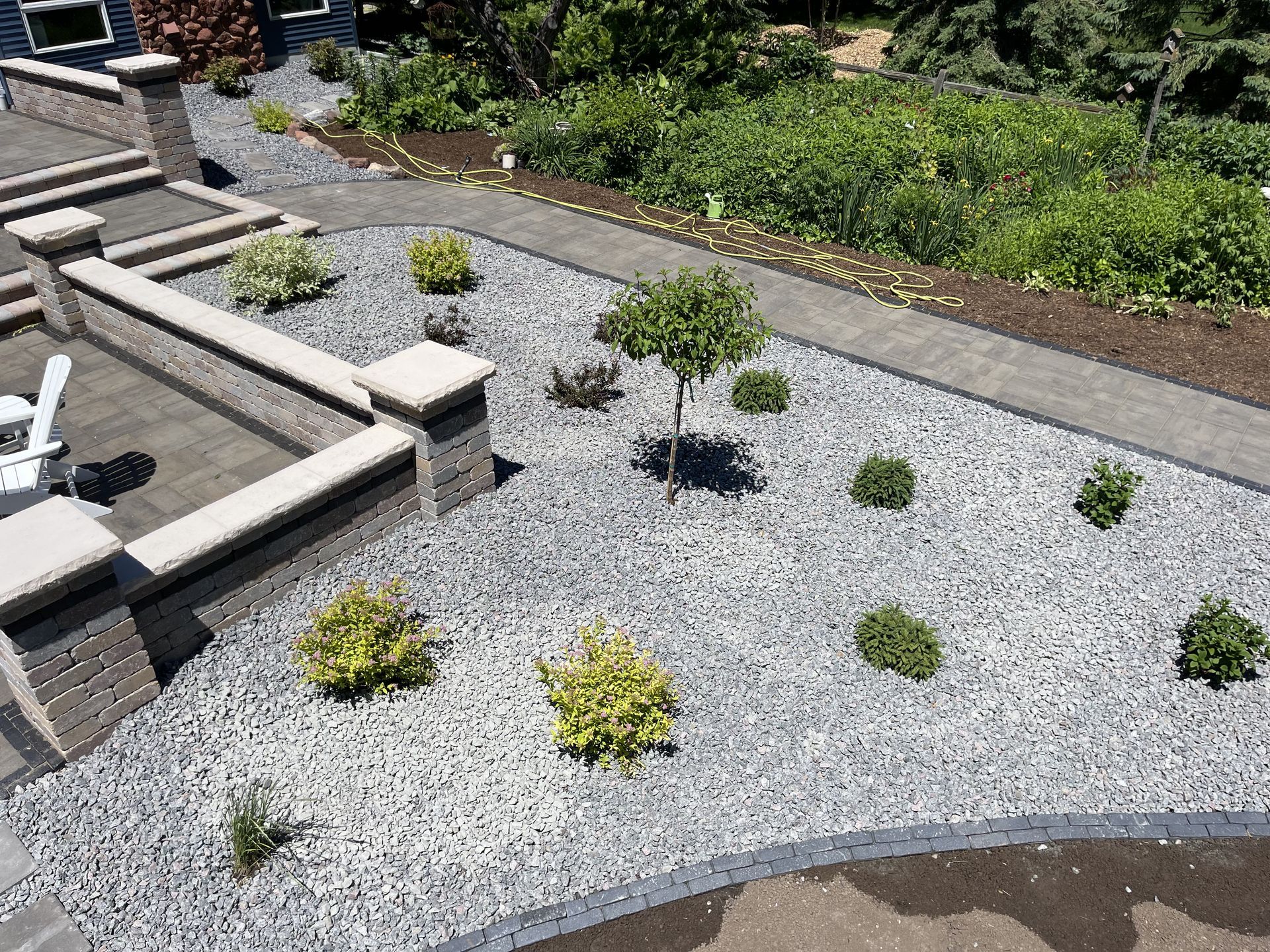 Gravel garden with small shrubs and a stone patio wall on the left