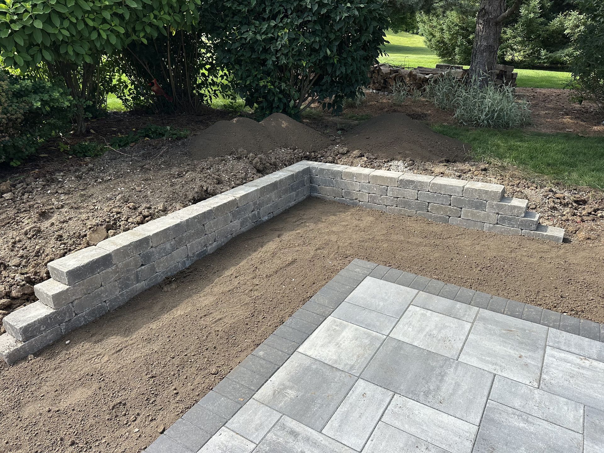 Backyard retaining wall under construction beside a paved patio and dirt grading area
