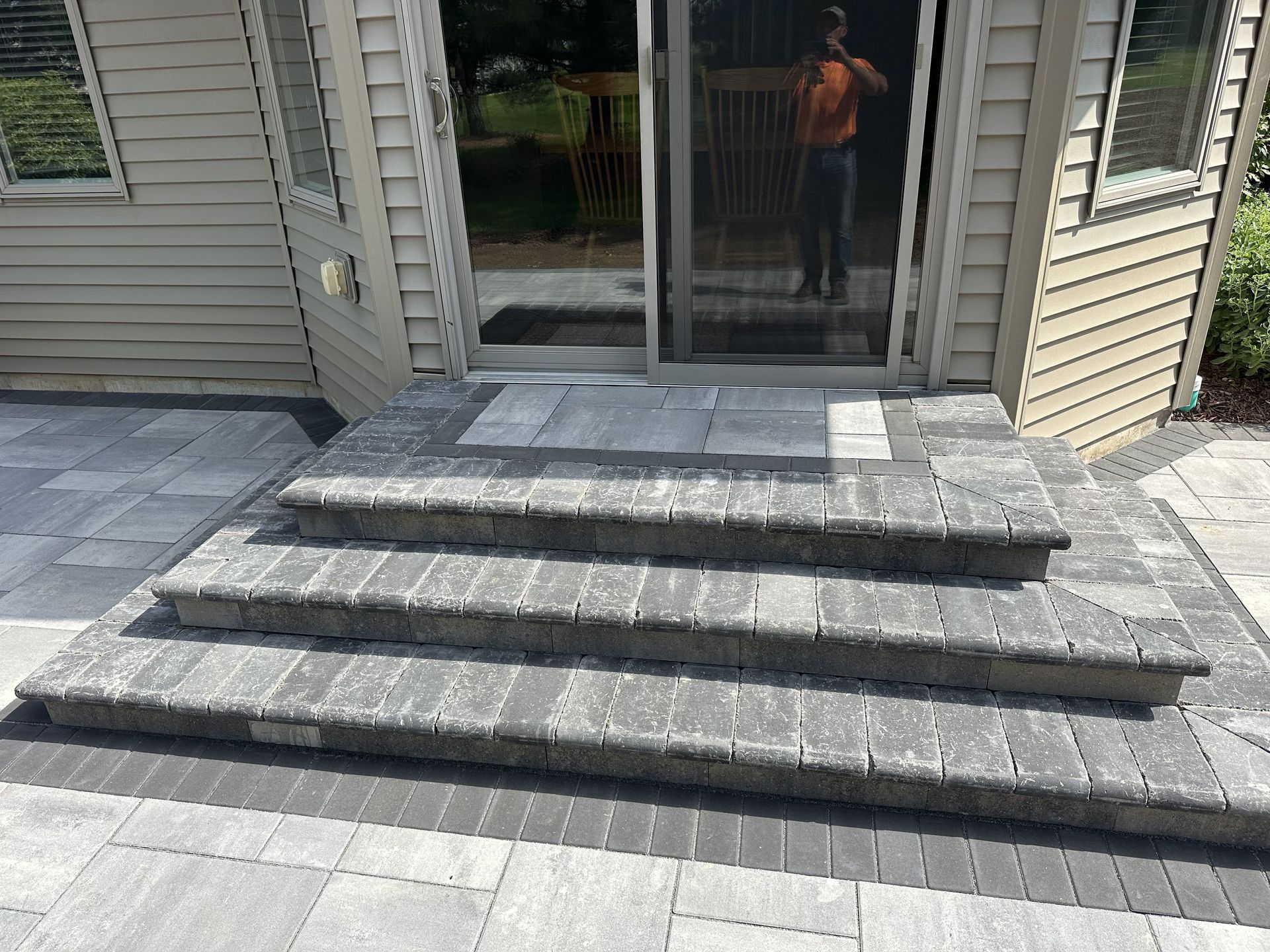 Front steps with dark stone pavers leading to a sliding glass door on a house exterior.