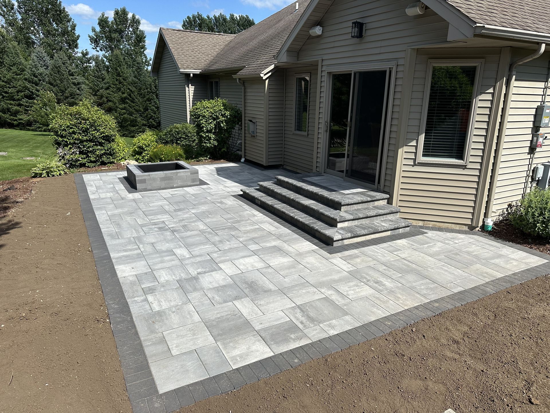 Stone patio with steps leading to a house entrance, bordered by gravel and a raised planter