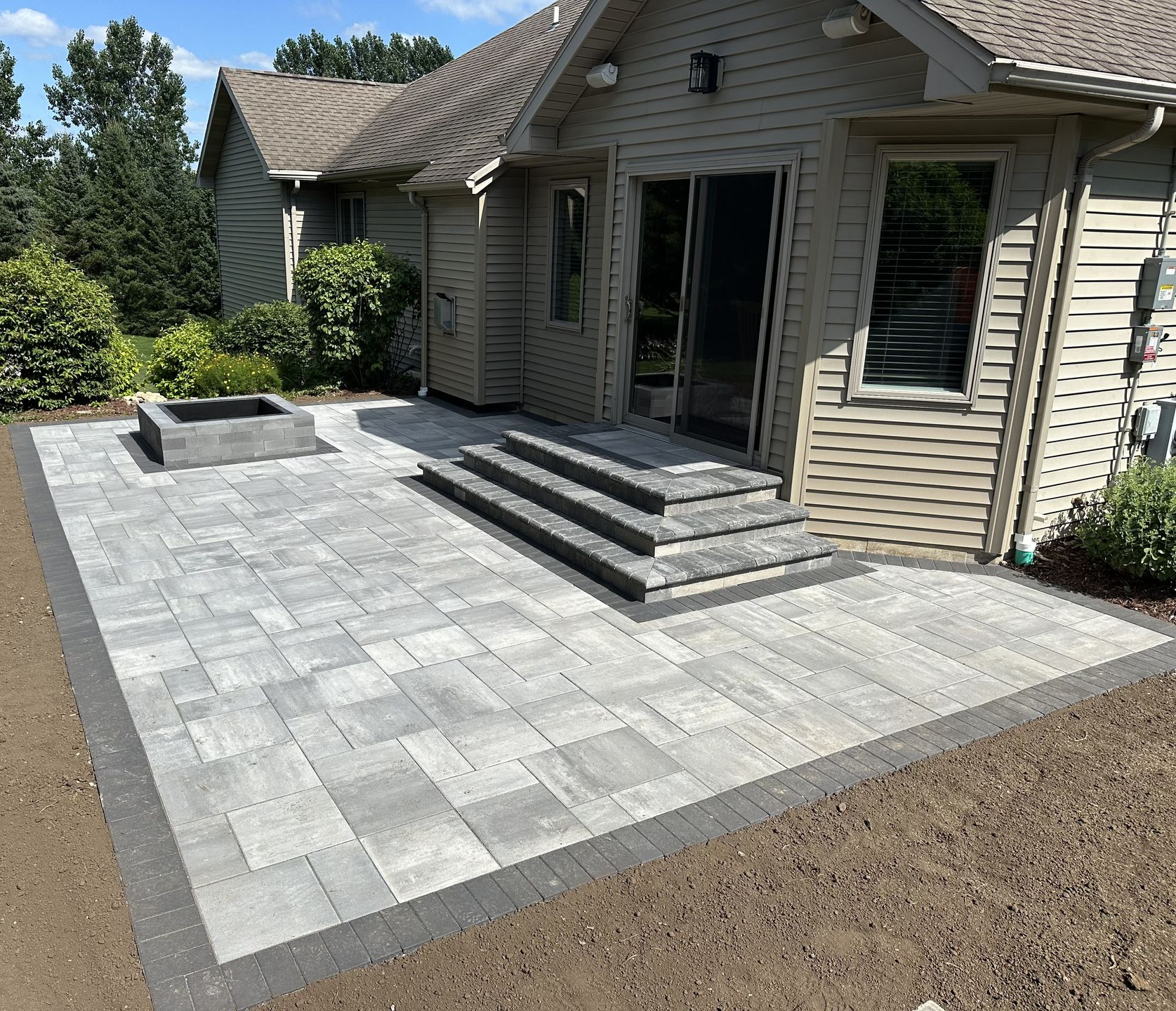 Back patio with gray pavers and steps leading to a beige house entrance