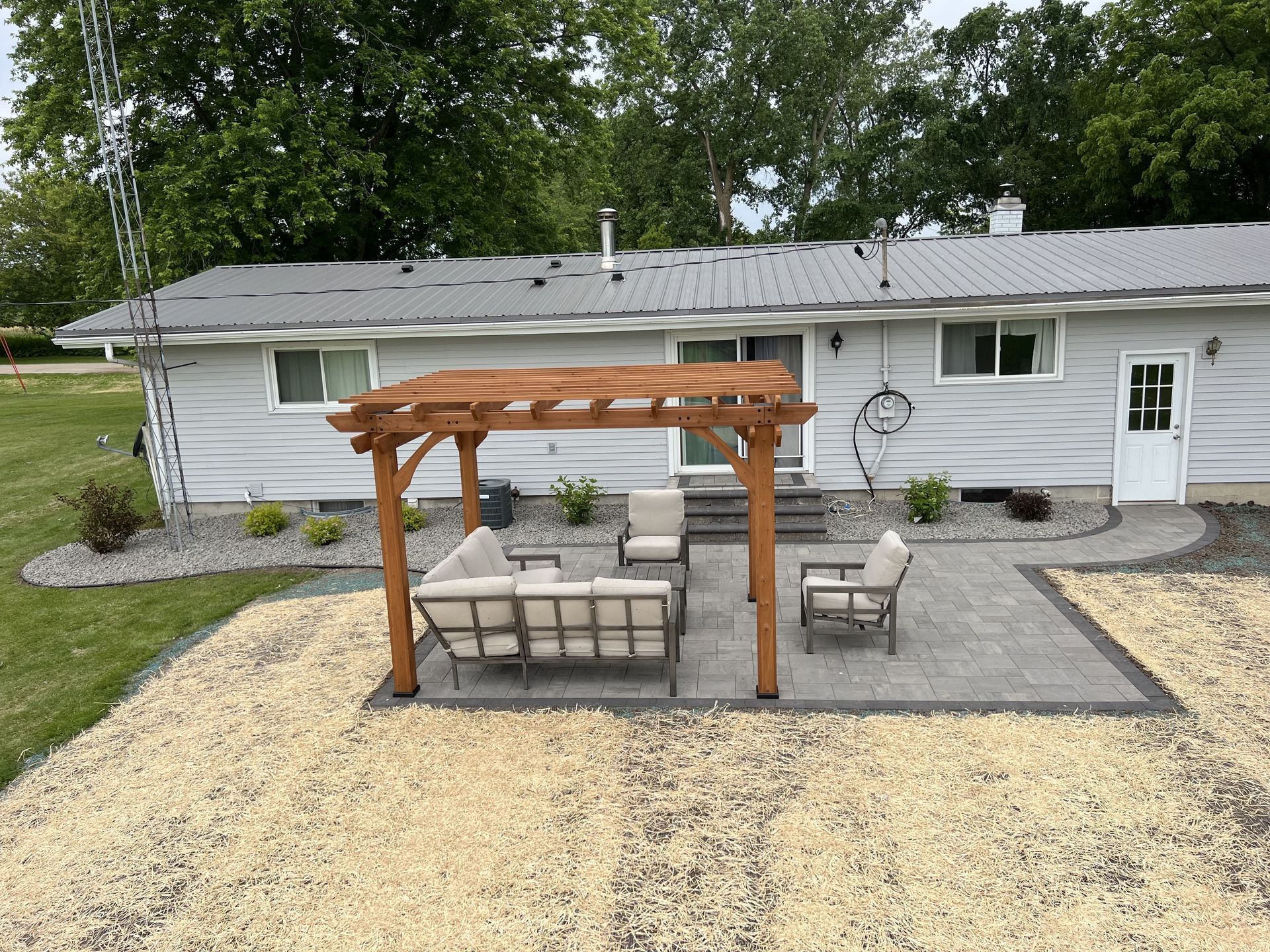 Backyard patio with pergola over outdoor seating beside a light gray house and gravel path
