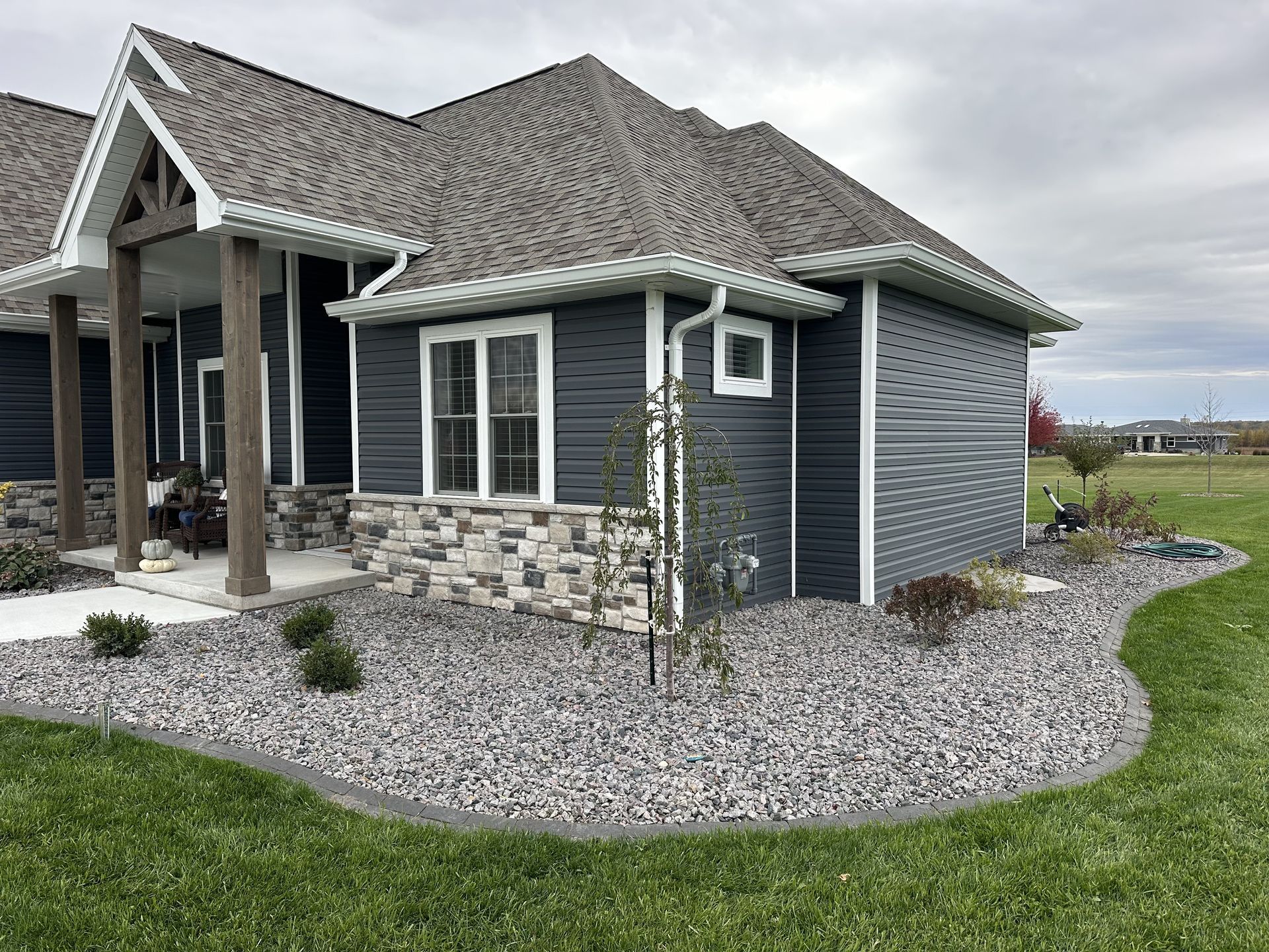 Lakeside yard with stone walkway, patio, dock, and lawn beside a gravel shore