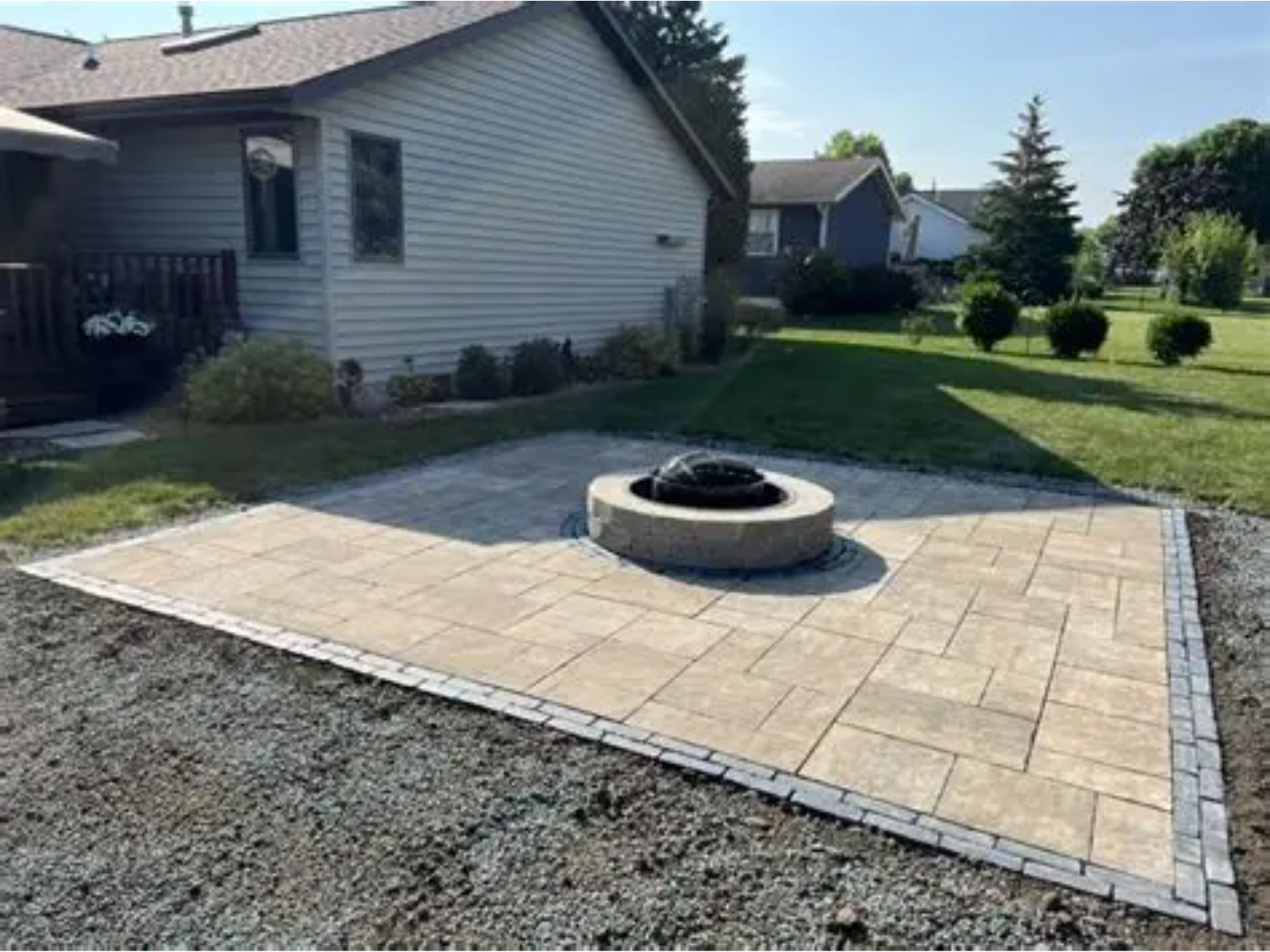 Backyard patio with stone pavers and a circular fire pit beside a house and lawn
