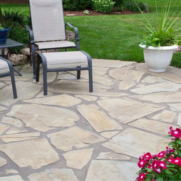 Patio with stone paving, lounge chairs, a white potted plant, and pink flowers by a green lawn