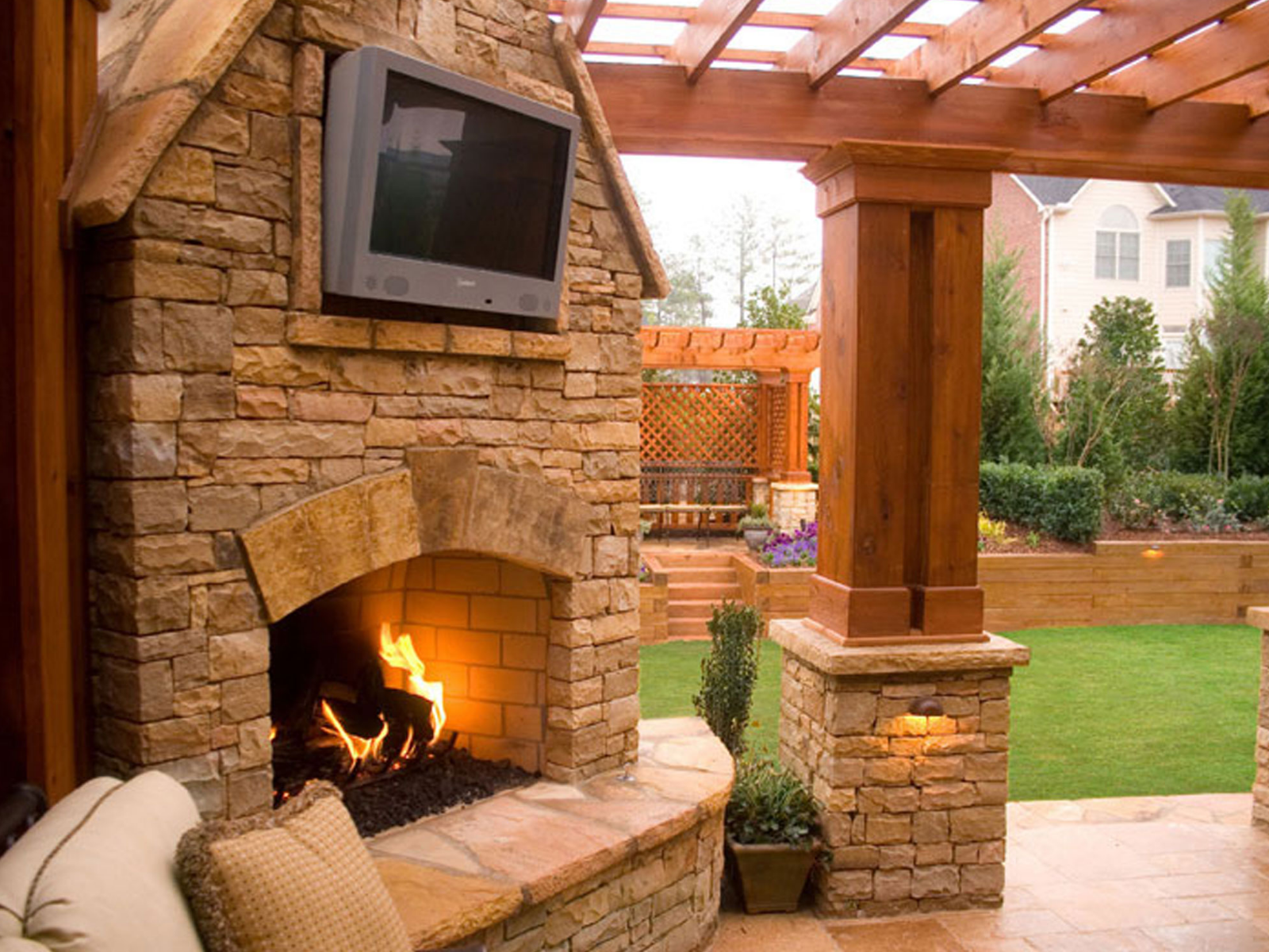 Stone outdoor fireplace with pergola and TV for backyard entertaining