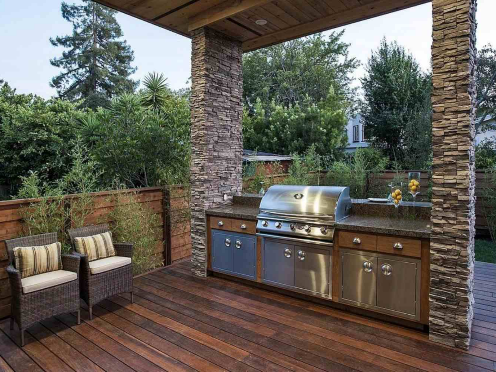 Outdoor patio with stone outdoor kitchen, stainless steel grill, and wicker seating under a wooden roof