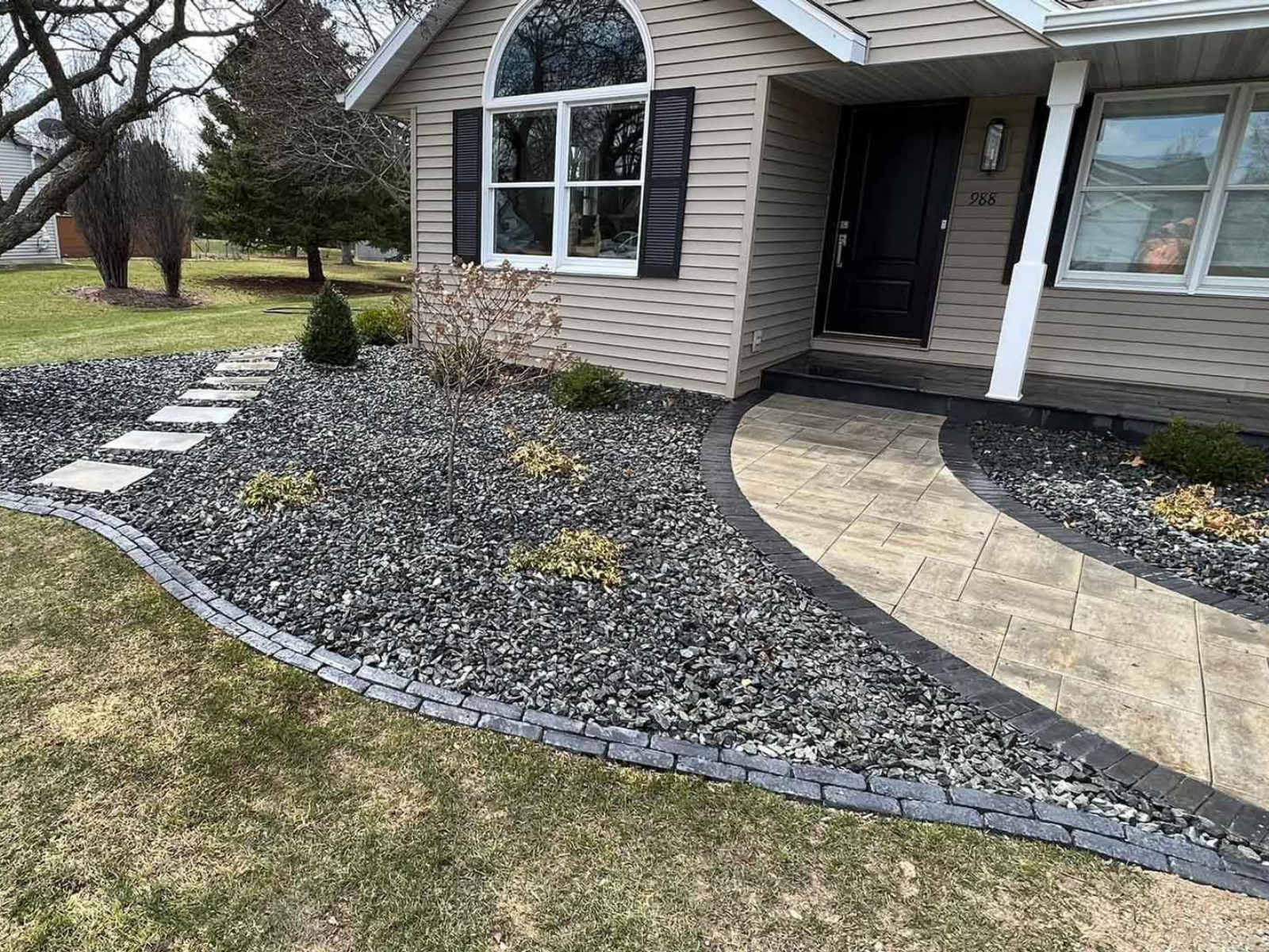 Front yard with curved stone walkway, gray gravel landscaping, and beige house exterior.