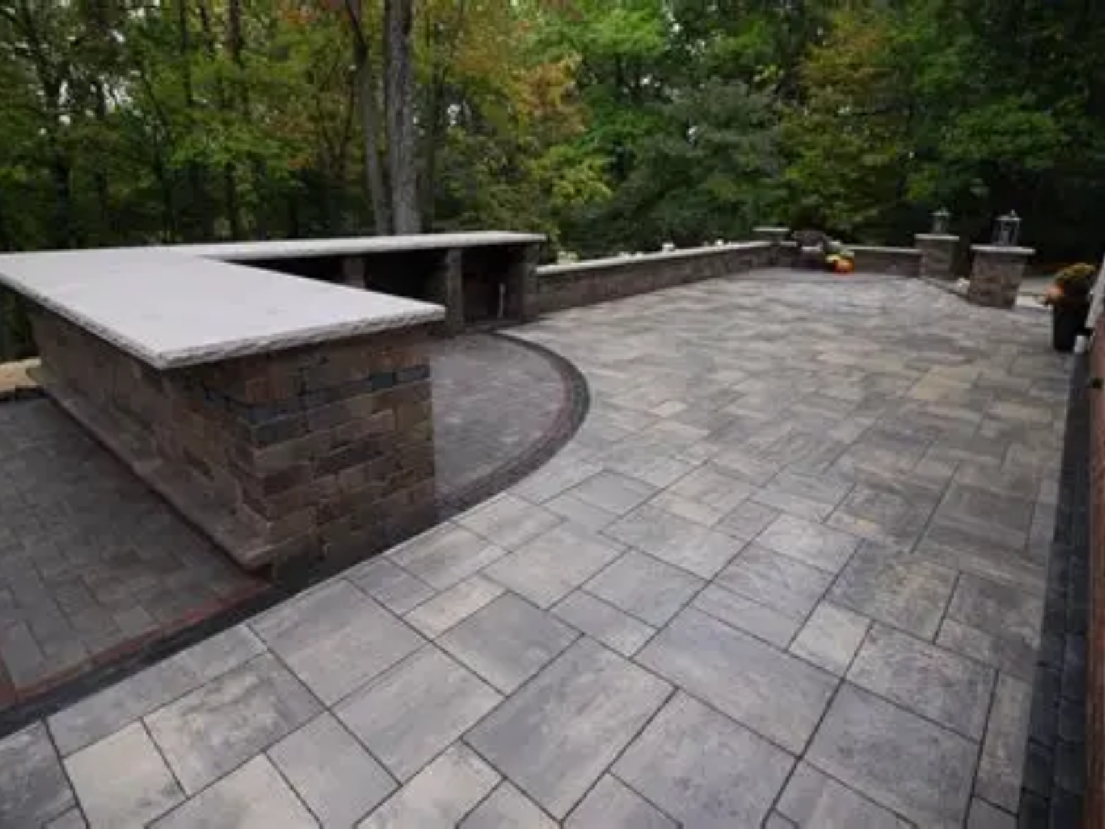 Stone patio with curved retaining wall and benches in a wooded outdoor area