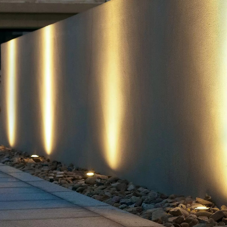 Outdoor walkway beside a wall lit by warm vertical lights at night
