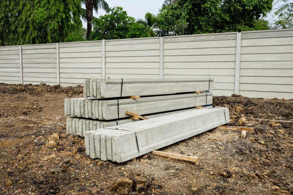 A Pile Of Concrete Poles Sitting On Top Of A Dirt Field Next To A Fence — Ingham Concrete–Icon in Ingham, QLD