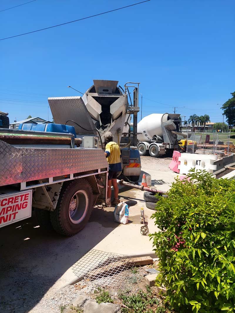 A Man Is Standing Beside A Concrete Mixer Truck — Ingham Concrete–Icon in Ingham, QLD
