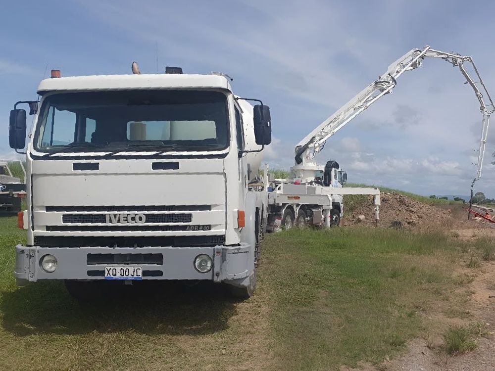 A White Iveco Concrete Mixer Truck Is Parked In A Grassy Field — Ingham Concrete–Icon in Ingham, QLD