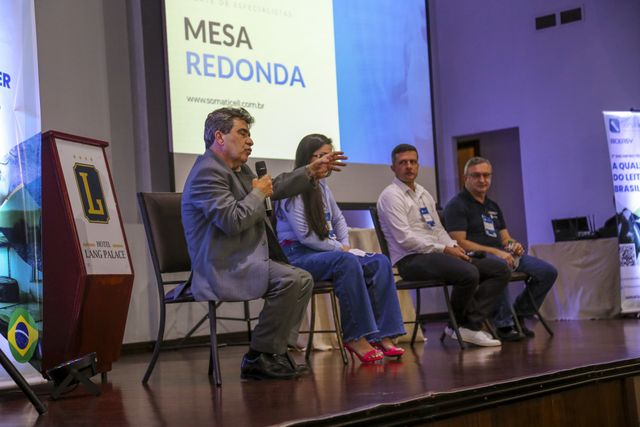 Quatro homens sentados em um painel de discussão no palco