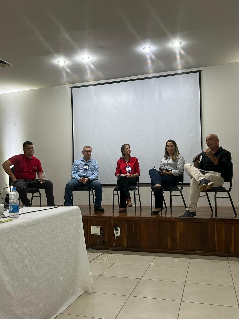 Mesa redonda com cinco palestrantes sentados em um pequeno palco em uma sala de conferências.