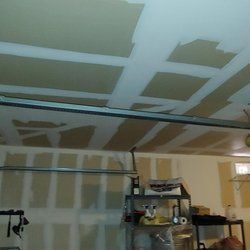 A garage with a garage door open and a ceiling that is being painted.