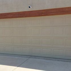 A beige garage door with a wooden trim on the side of a house.