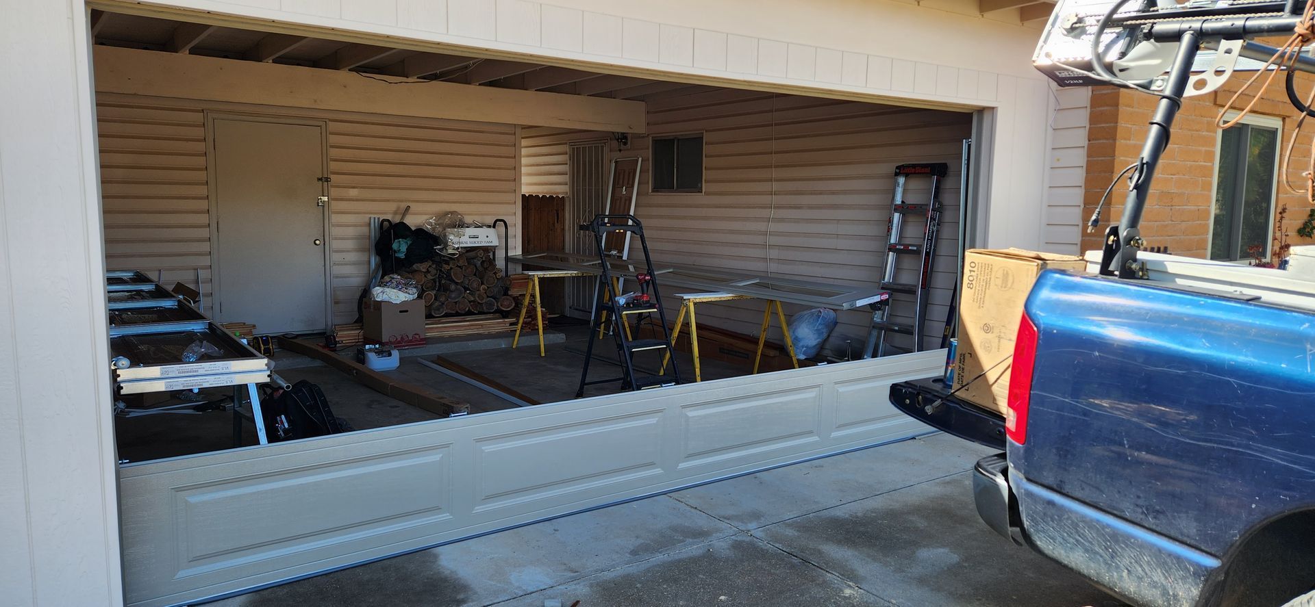 A blue truck is parked in front of a garage door that is being opened.