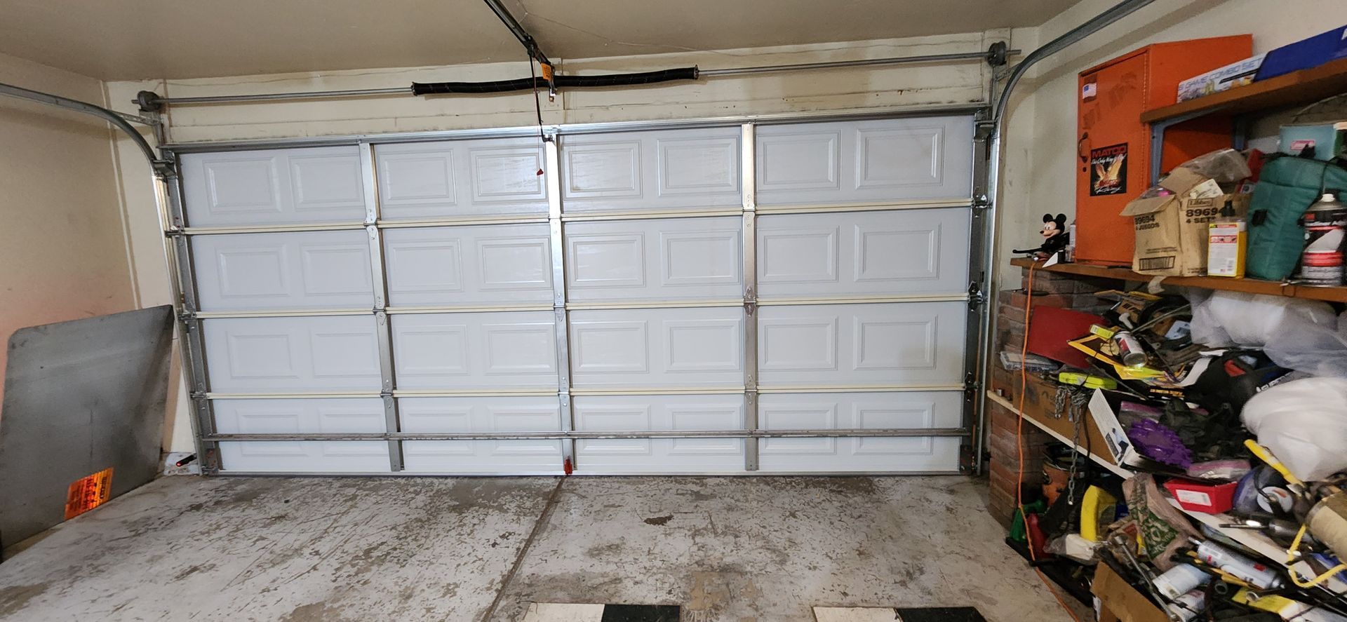 A garage filled with lots of junk and a garage door open.