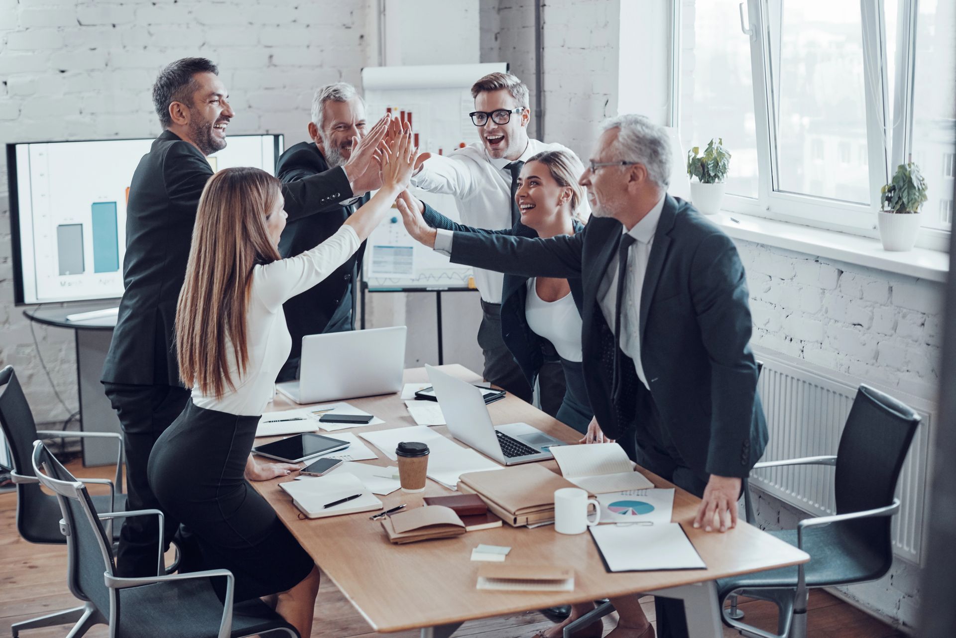 Colleagues high-five around a conference table in a bright office meeting room