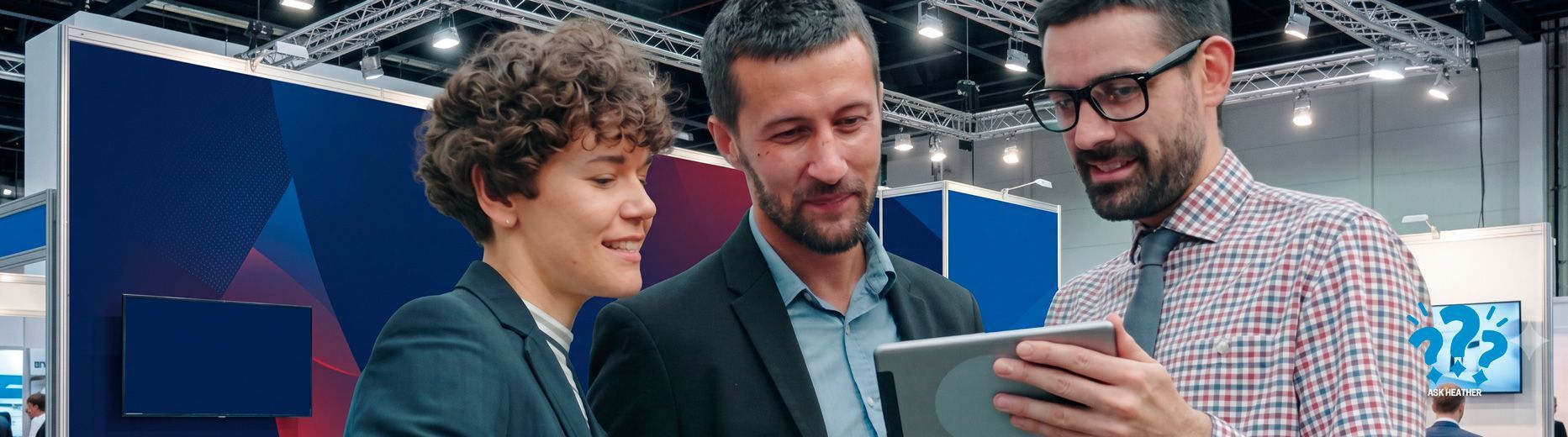 Three people in business attire reviewing a smartphone at a tech conference booth