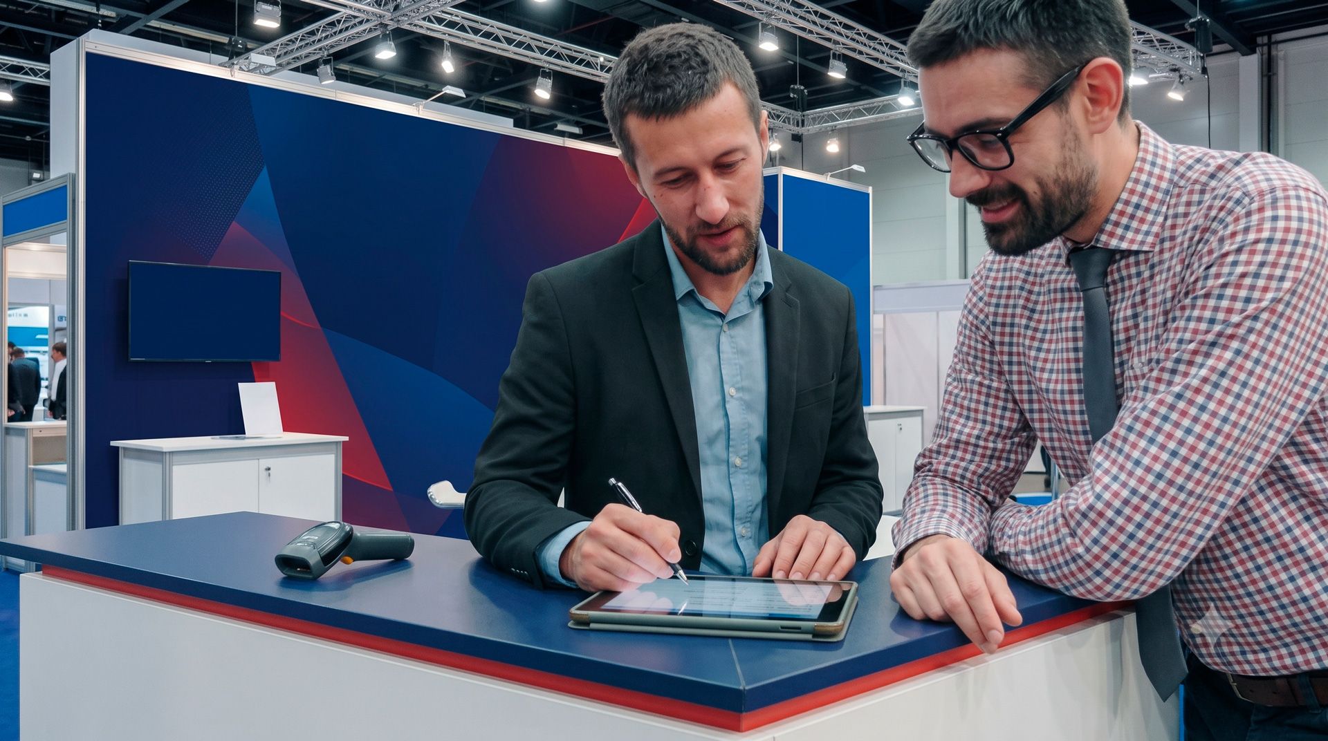 Two men reviewing a tablet at a trade show booth with blue and red displays
