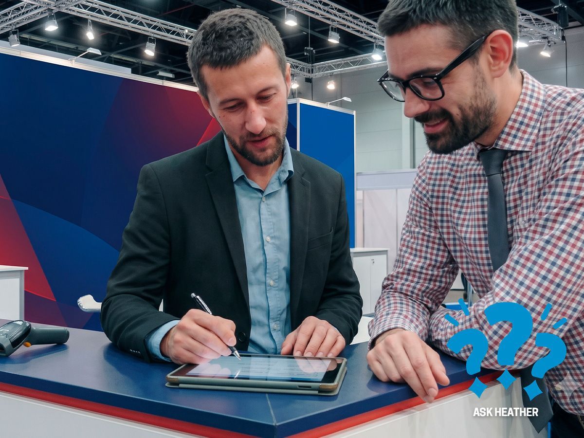 Three coworkers reviewing a tablet at a trade show booth, smiling and discussing ideas.