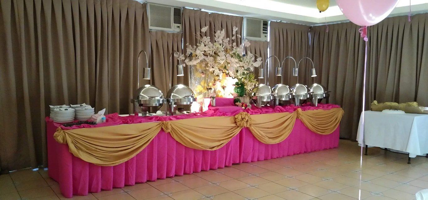 A long pink and gold buffet table with balloons in a room.