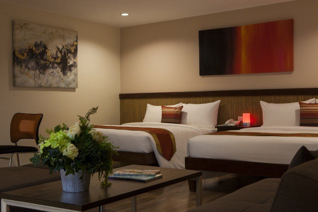 A hotel room with two beds , a coffee table and a vase of flowers.