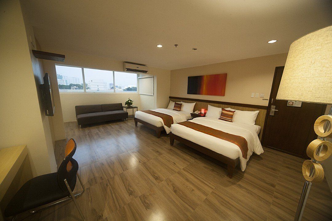 A hotel room with two beds , a couch and a lamp.