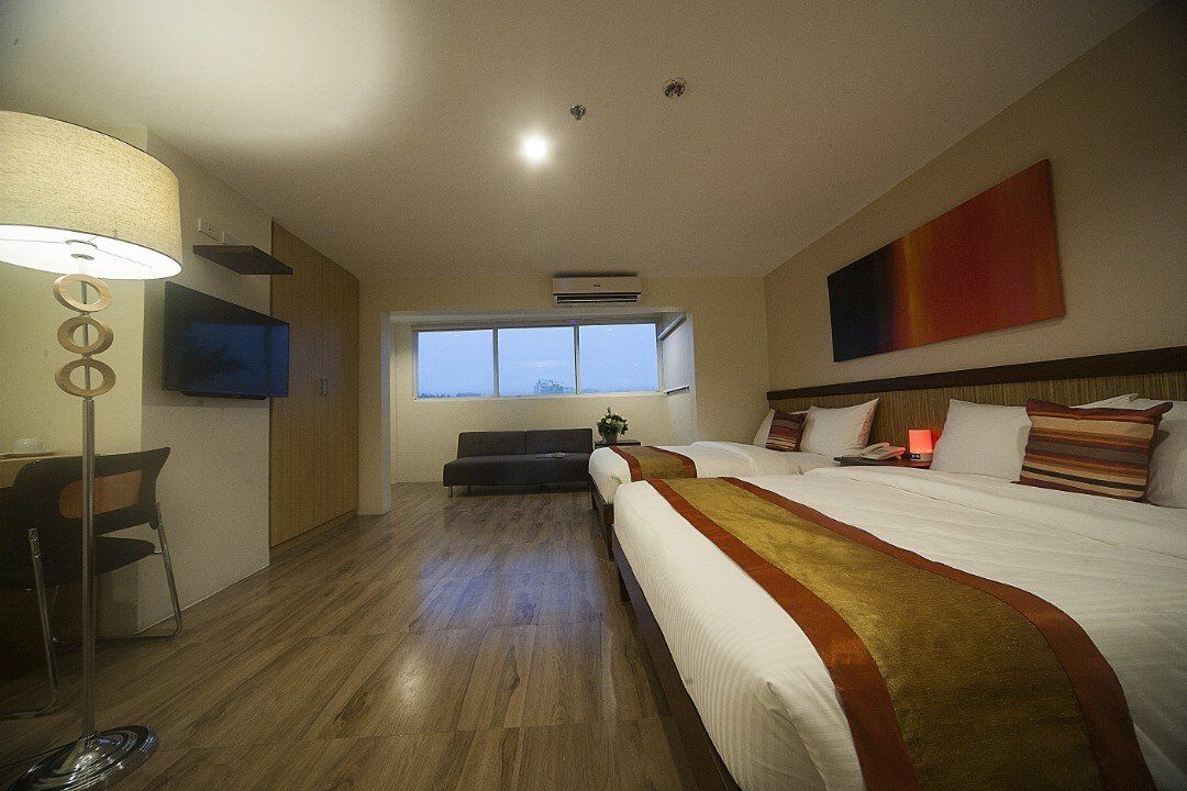 A hotel room with two beds , a couch , a lamp and a television.