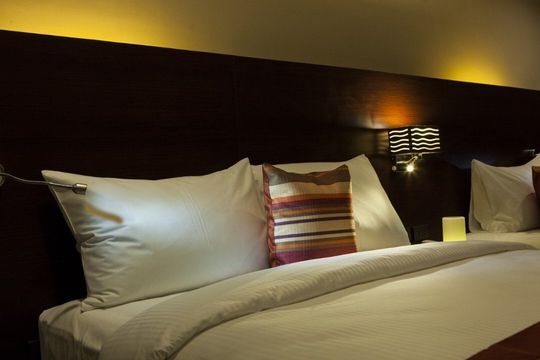 A bed with white sheets and pillows in a hotel room