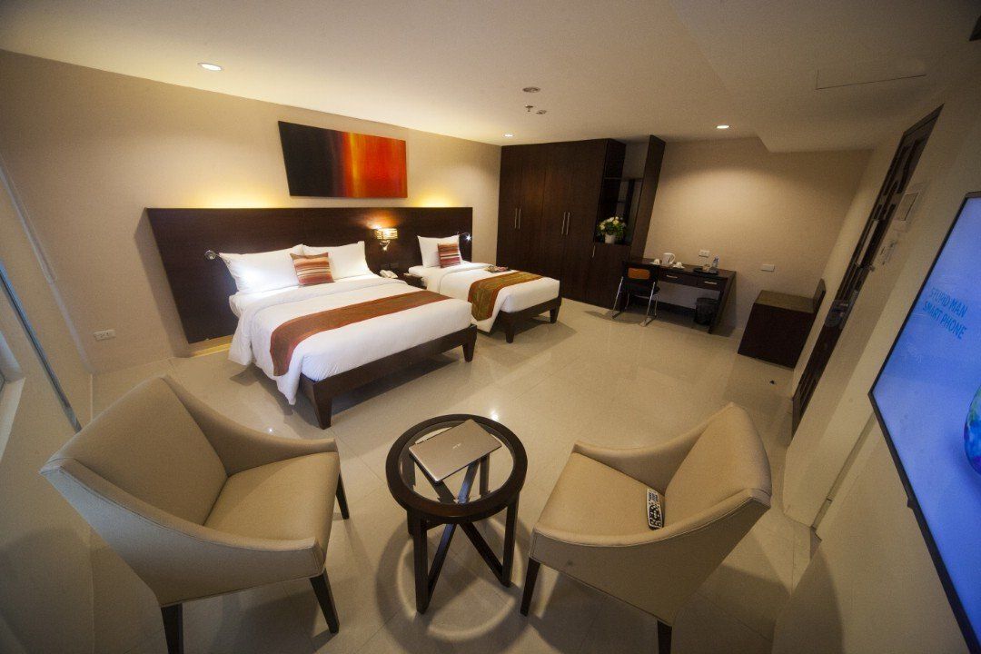 A hotel room with two beds , chairs , a table and a television.