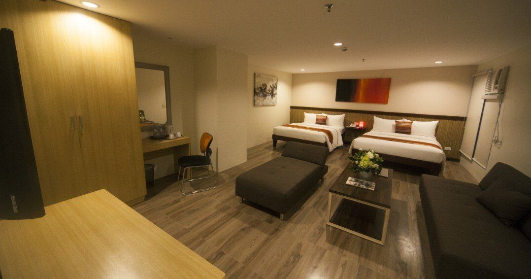 A hotel room with two beds , a couch , a table and a mirror.