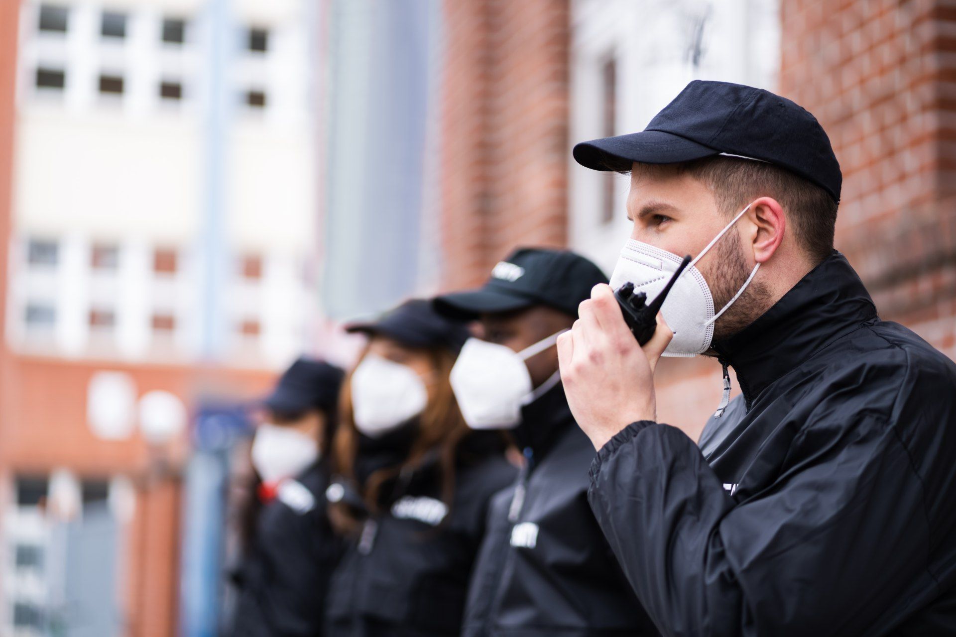 People wearing masks and hats, standing outside. One man speaks into a radio.