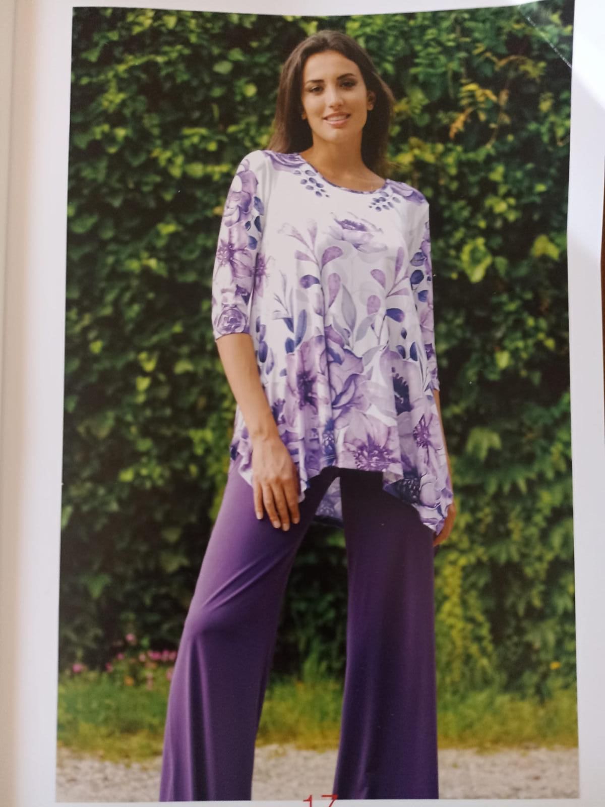 Una donna con pantaloni viola e un top fantasia posa all'aperto.