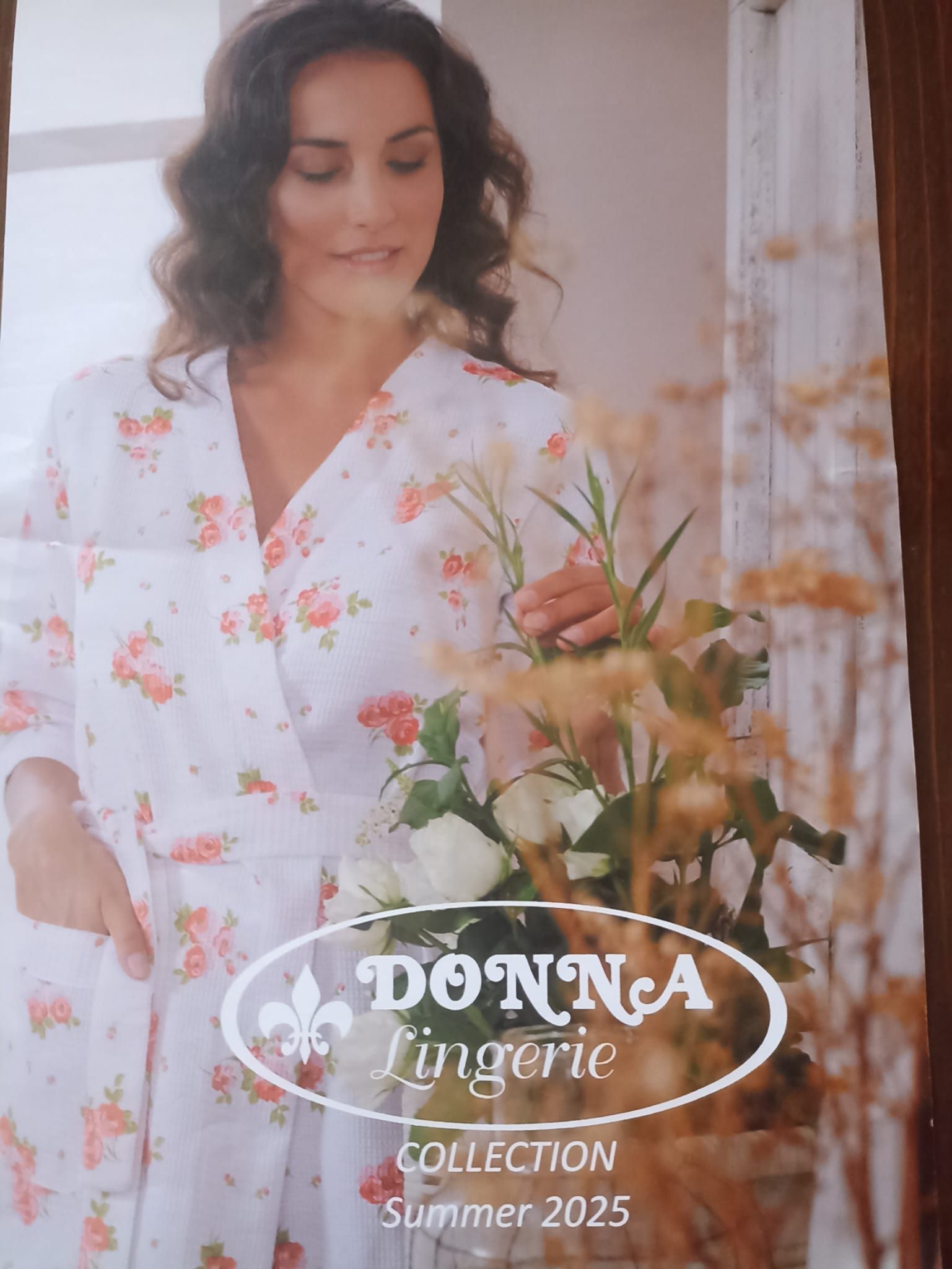 Donna in vestaglia floreale, con fiori in mano, per la collezione DONNA Lingerie Estate 2025.