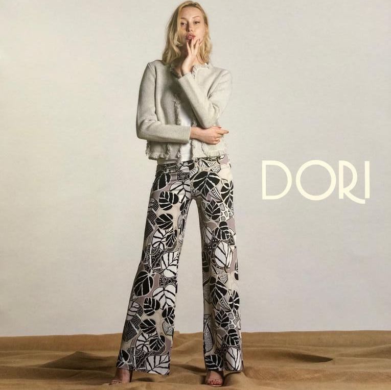 Donna con giacca leggera e pantaloni larghi stampati, in posa per una pubblicità di moda; sfondo beige.