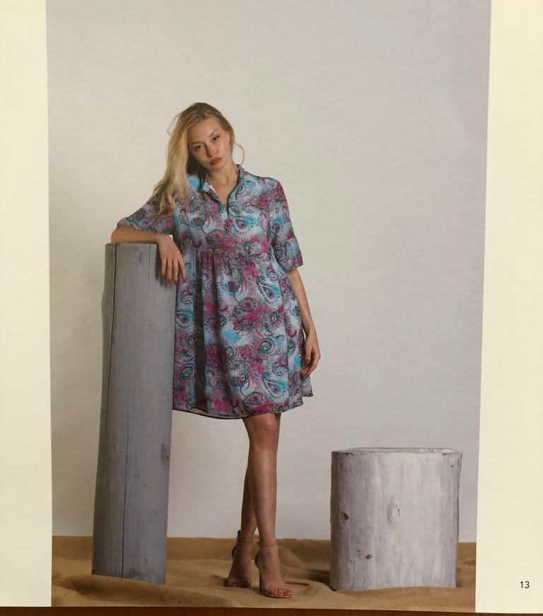 Donna in abito paisley appoggiata a un palo di legno in uno studio.
