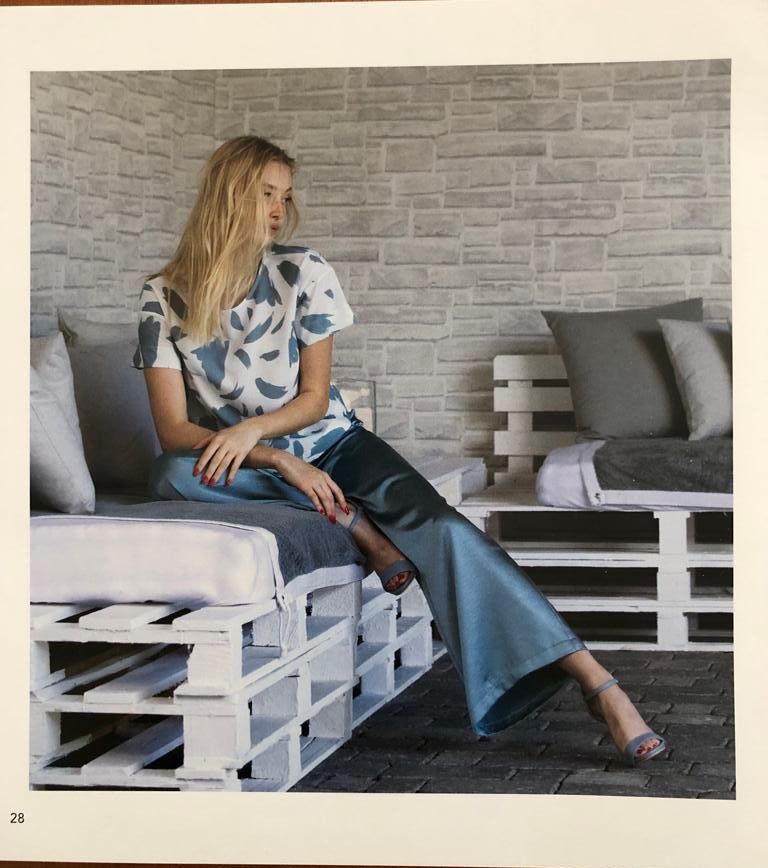 Una donna vestita di blu è seduta su un divano bianco fatto di pallet. Sullo sfondo un muro di mattoni chiari.