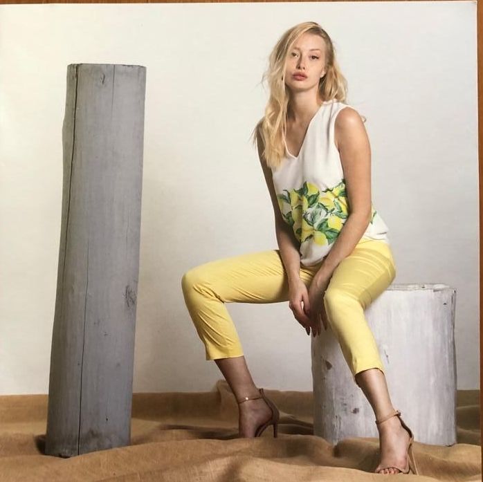 Donna seduta su un ceppo bianco, indossa pantaloni gialli e una maglietta a fiori; tacchi marroni.