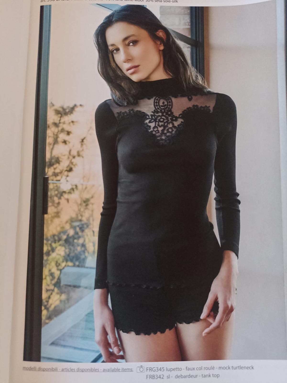 Donna in lingerie nera con dettagli in pizzo, in piedi vicino a una finestra.