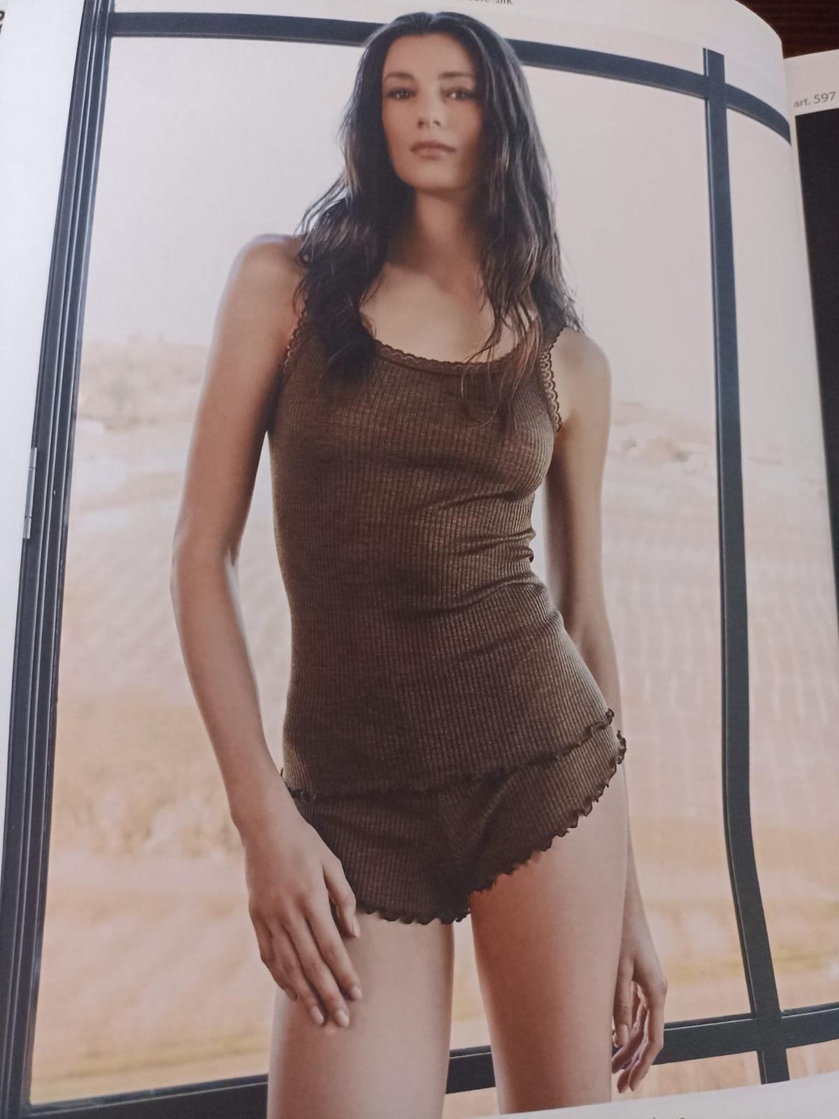 Donna che indossa una canottiera marrone e pantaloncini, in piedi vicino a una finestra.