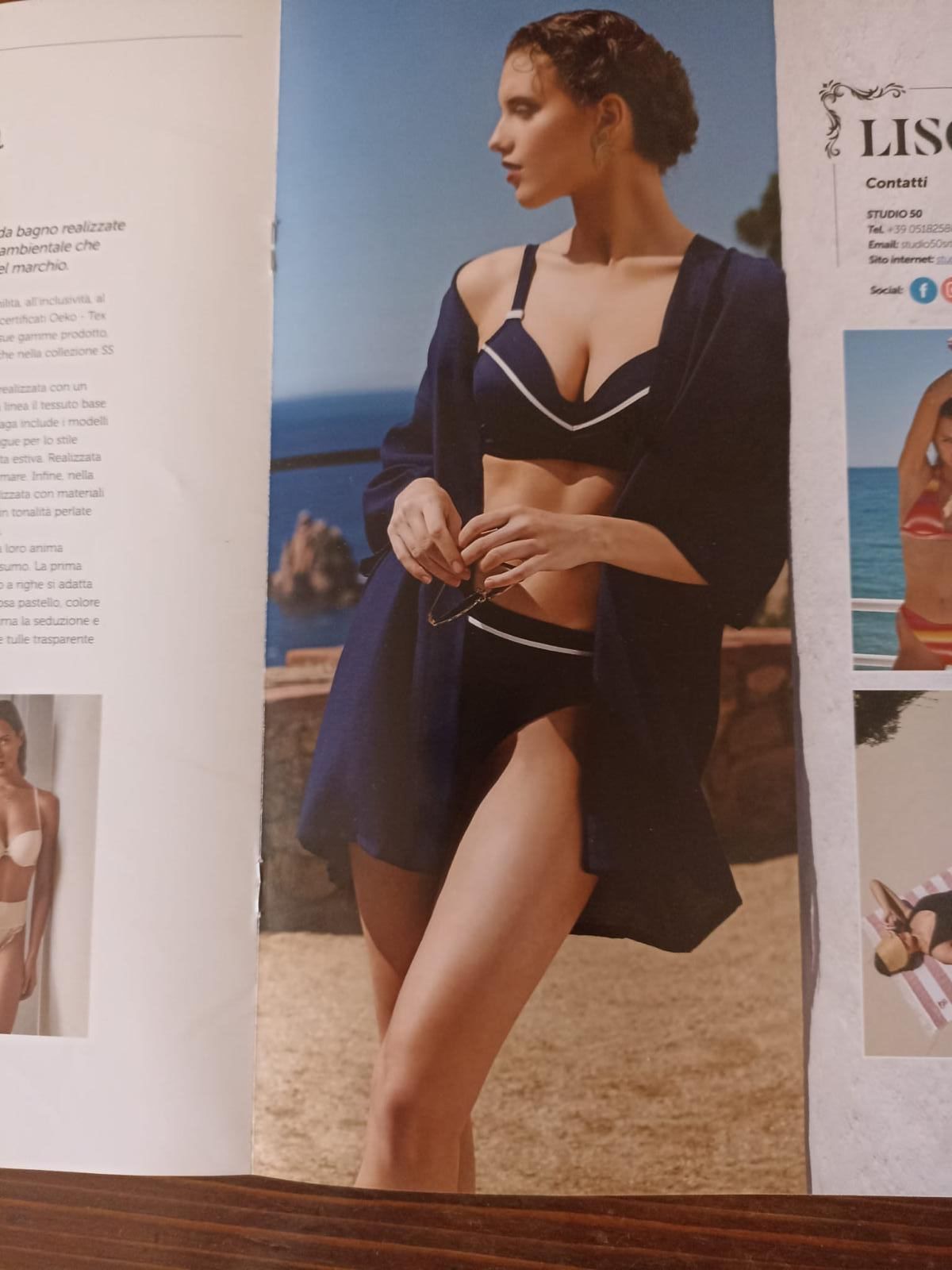 Donna in bikini blu navy e vestaglia, con in mano gli occhiali, che guarda altrove, all'aperto.
