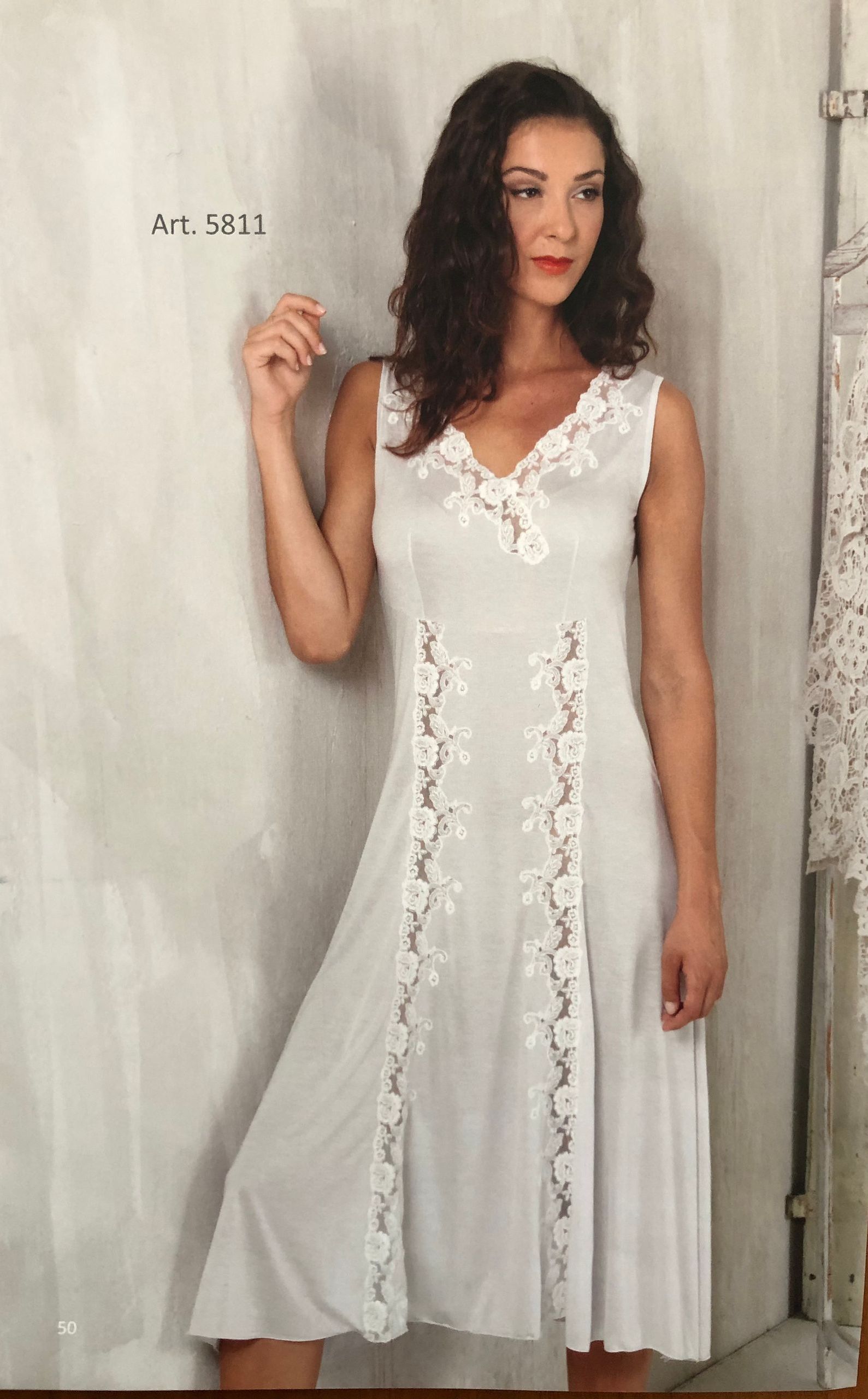 Donna in abito bianco con dettagli in pizzo, appoggiata a un muro.